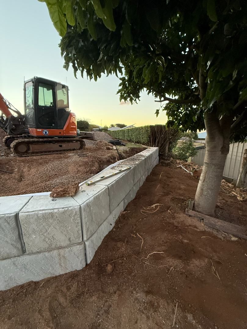 A Bulldozer is Sitting on Top of a Dirt Hill Next to a Tree — Ape Earthmoving In Westbrook, QLD