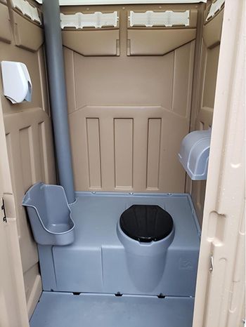 The inside of a portable toilet with a toilet and a trash can.