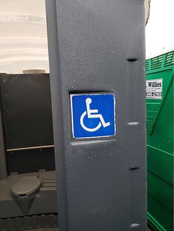 A handicap sign is on the side of a portable toilet.