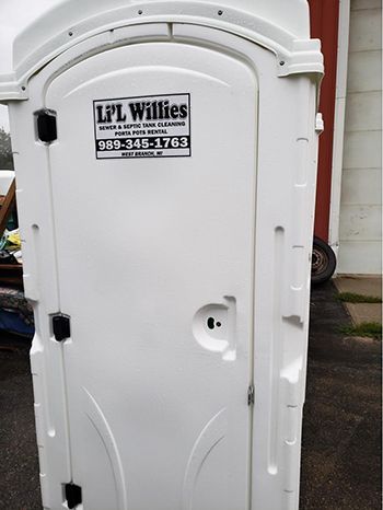 A white portable toilet with a sticker on the door that says lpl willies.