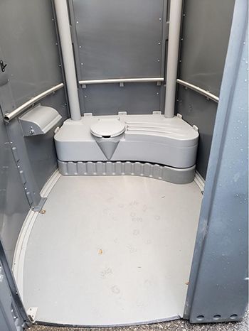 The inside of a portable toilet with a toilet and a trash can.