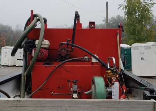 A red tank with a hose attached to it is on the back of a truck.