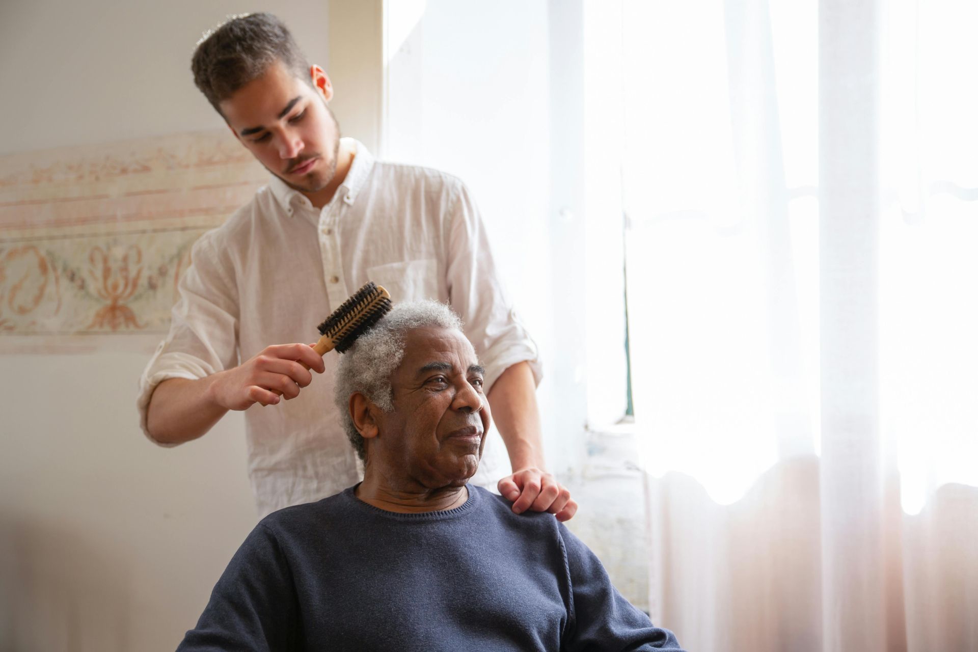 A young man is brushing the hair of an older man.