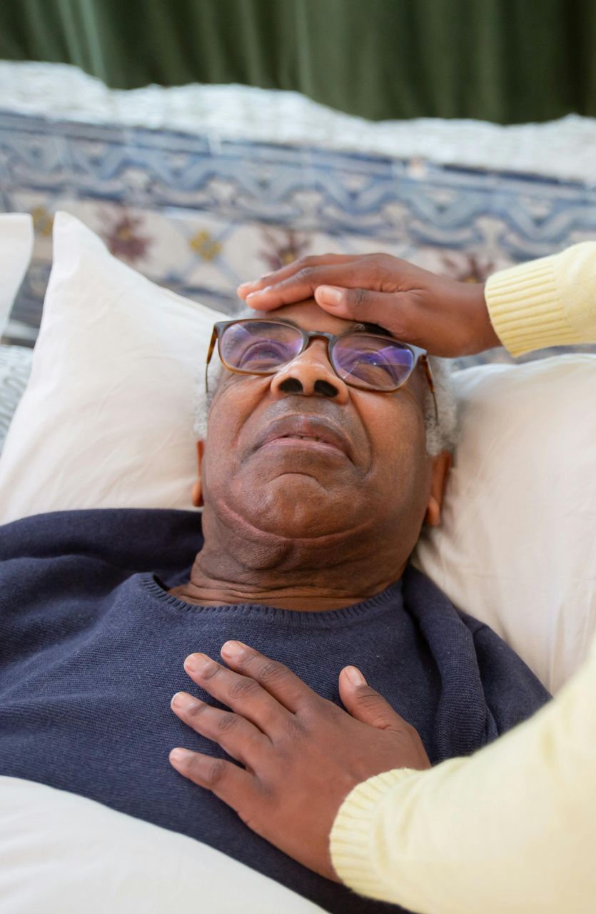 An elderly man is laying in a bed with a nurse touching his forehead.