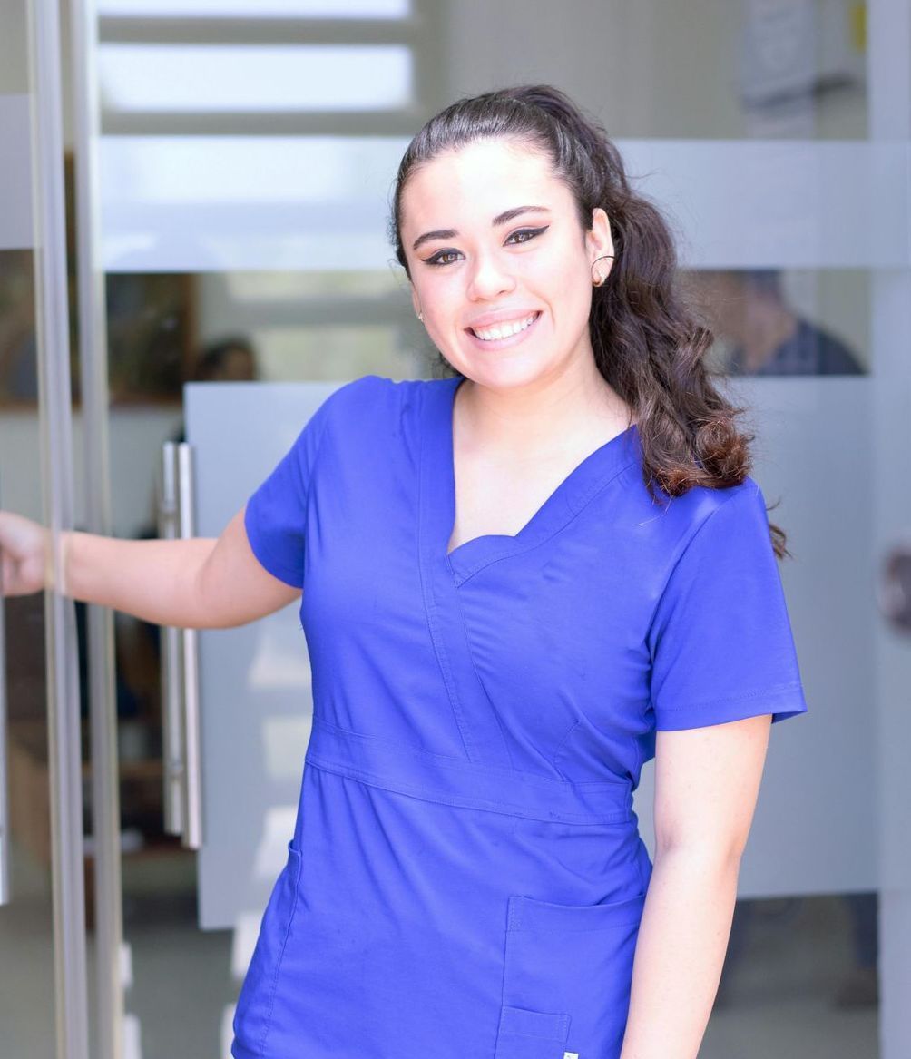 A woman in a blue scrub top is standing in front of a glass door