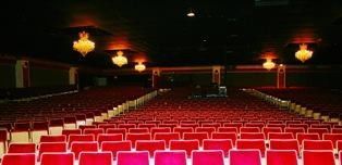 An empty theater with rows of red seats and chandeliers.