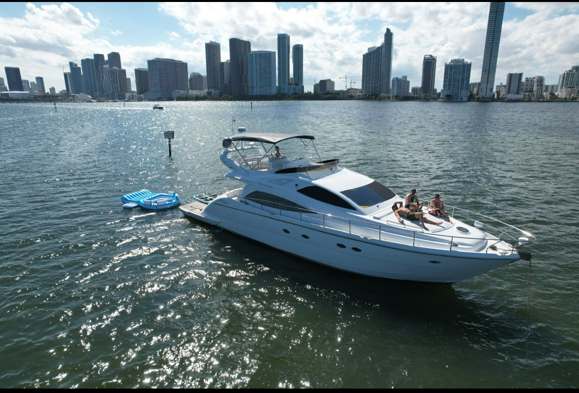 An aerial view of a yacht in the water with a city skyline in the background.