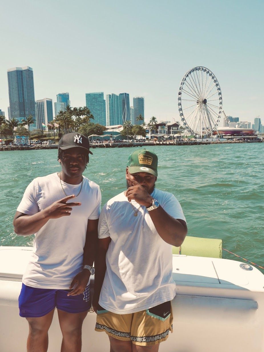 Two men are standing on a boat with a ferris wheel in the background.
