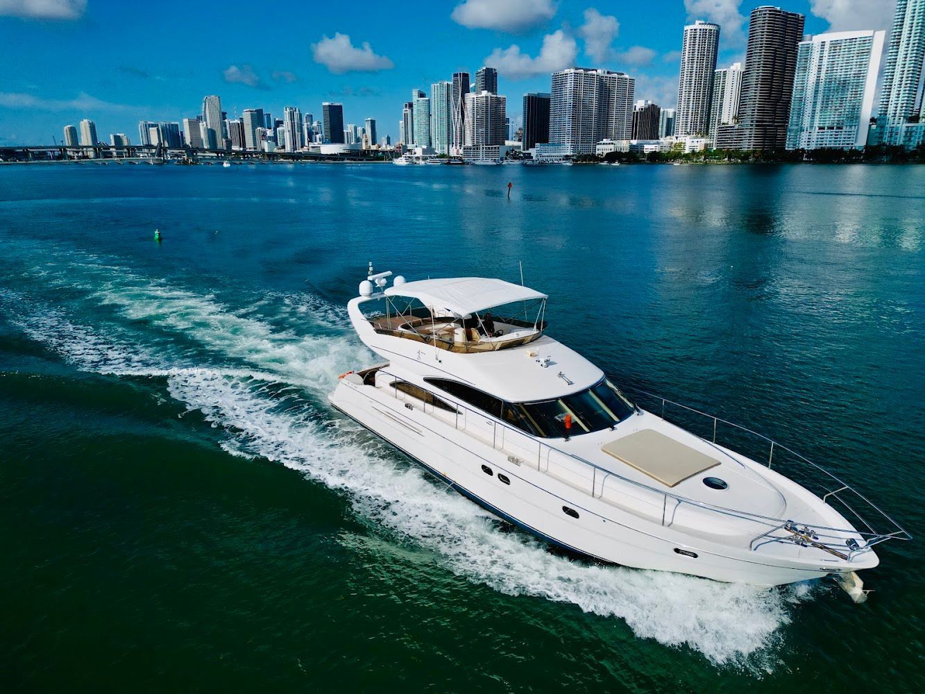 A white yacht is floating on top of a body of water with a city skyline in the background.