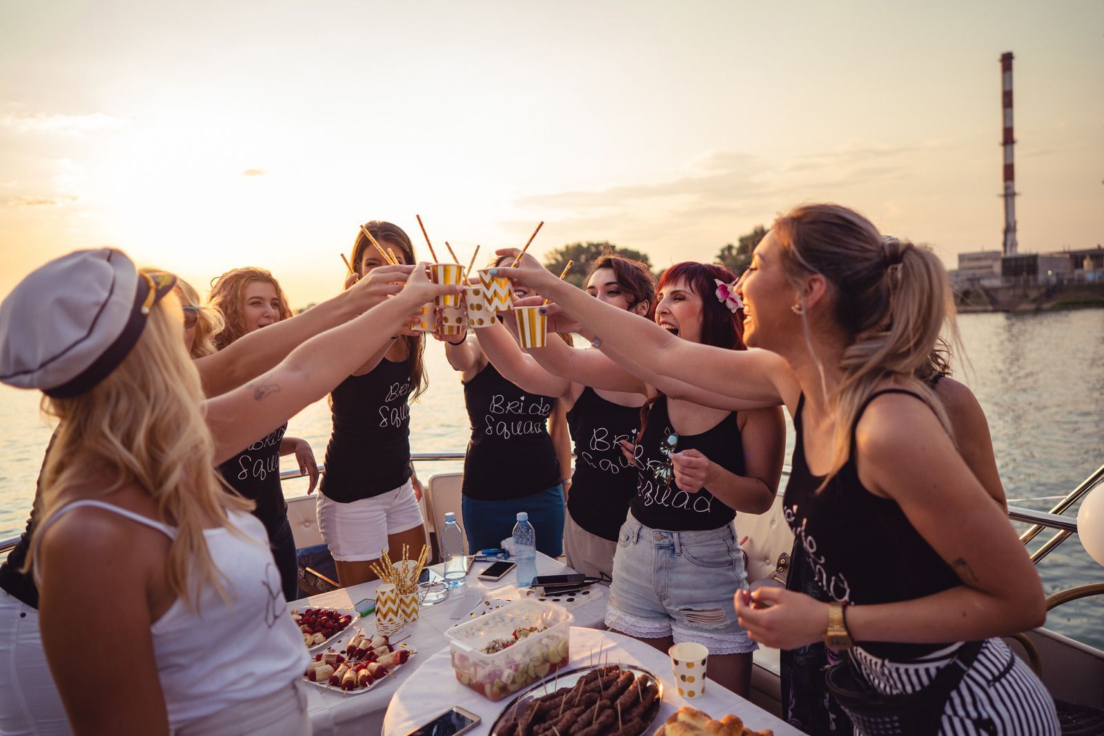 Group of women on a boat toasting drinks at sunset.
