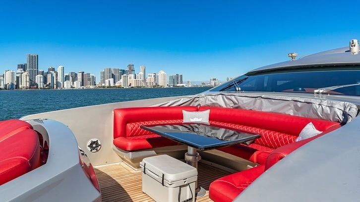 The back of a yacht with red seats and a table with a city skyline in the background.