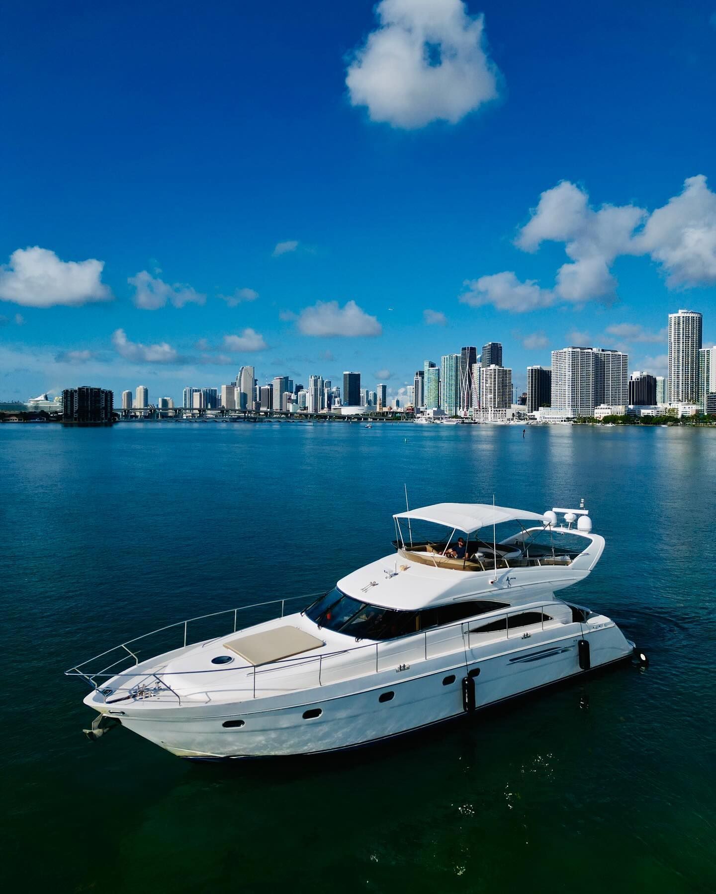 An aerial view of a yacht in the water with a city skyline in the background.