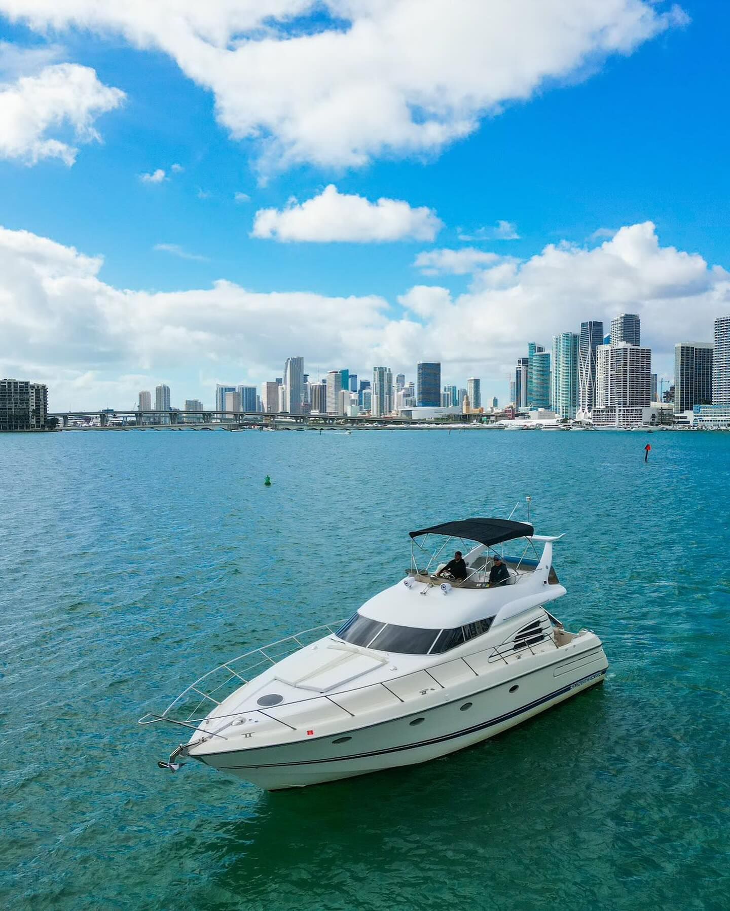 A white yacht is floating on top of a body of water with a city skyline in the background.
