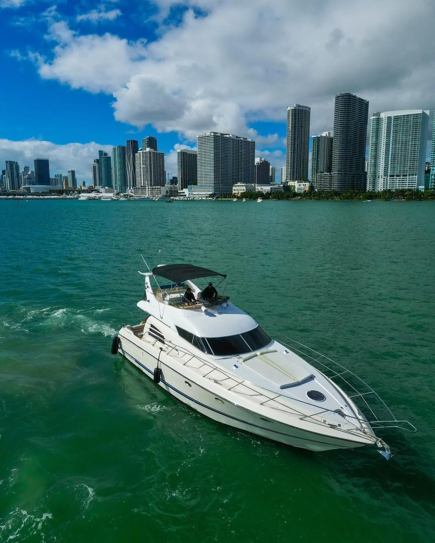 An aerial view of a yacht in the water with a city skyline in the background.