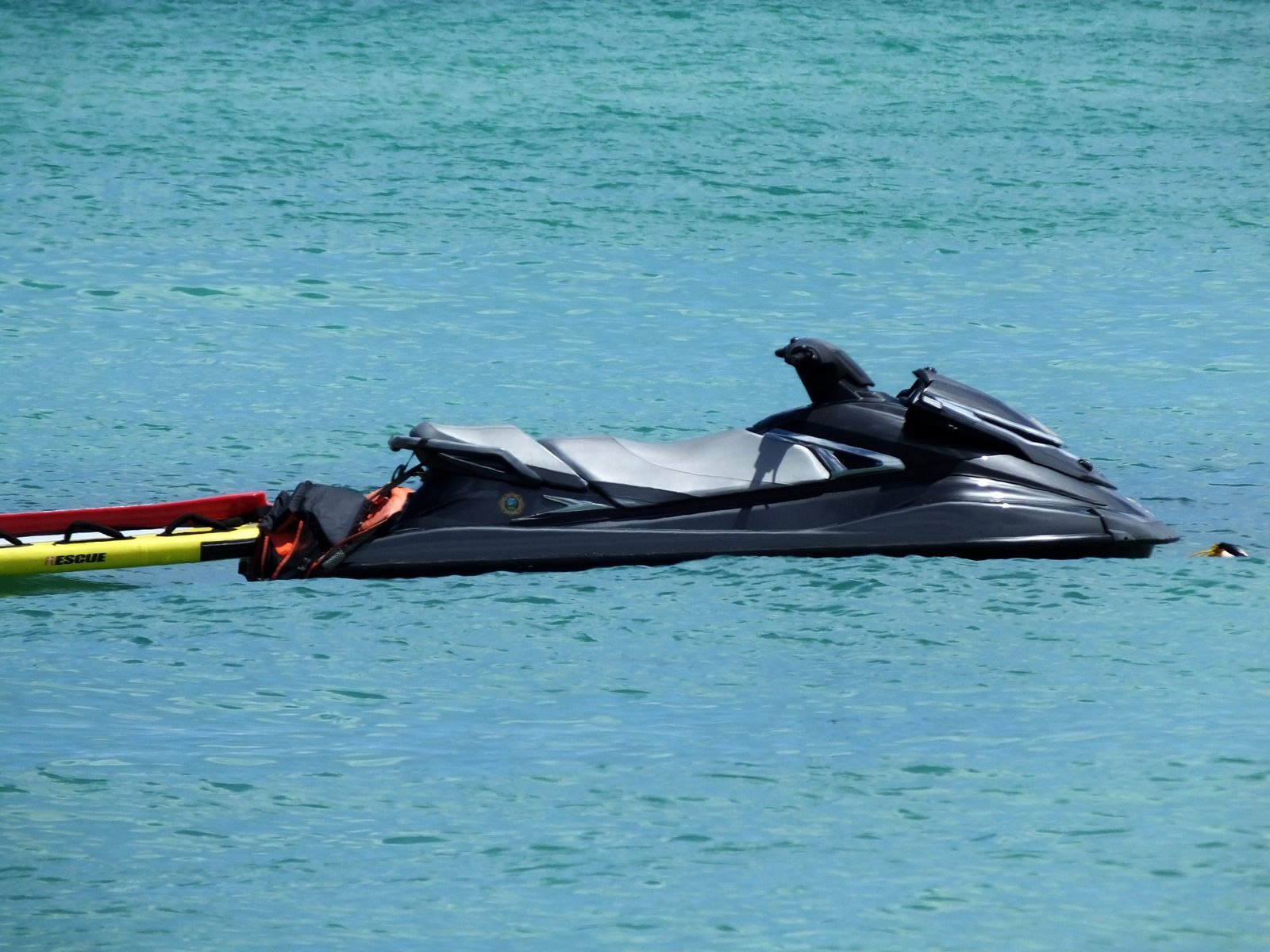 Black jet ski floating on blue water. Yellow and red tube partially visible.