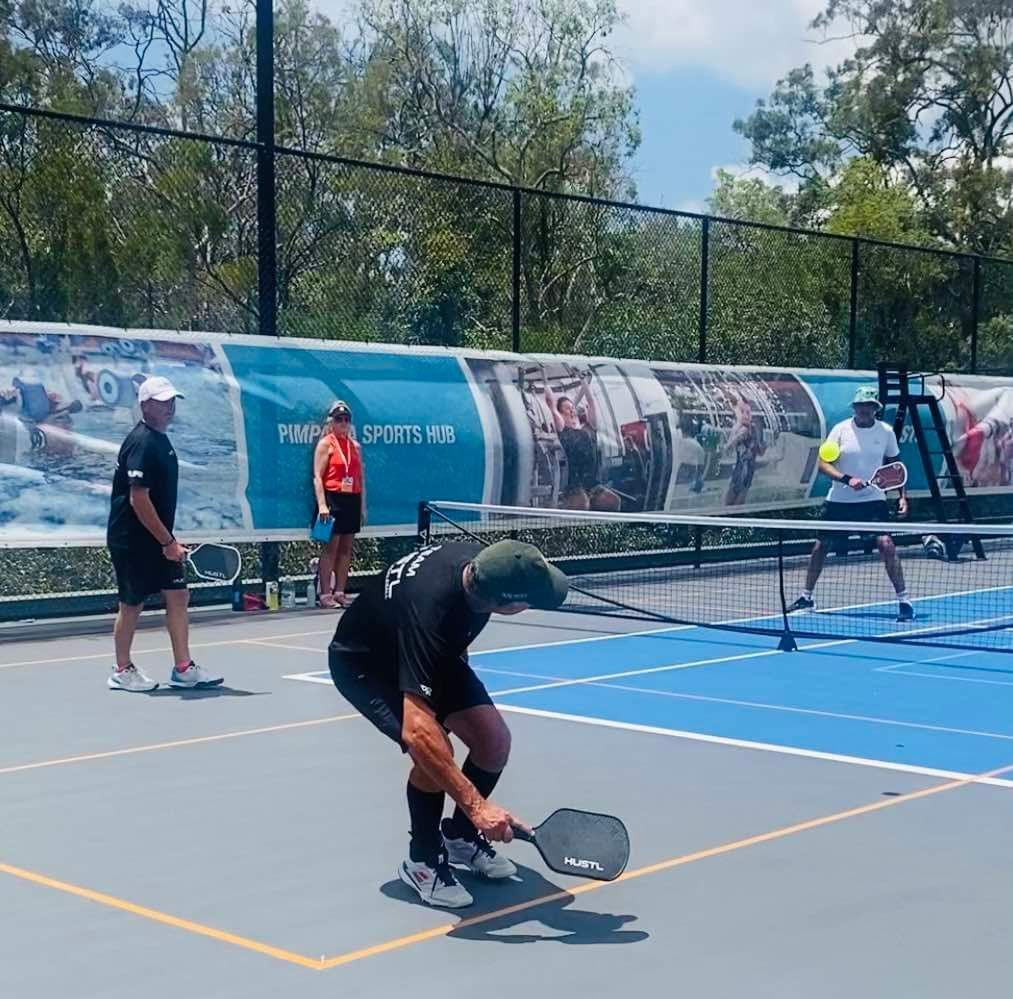 A group of people from Gold Coast Pickleball are playing a game of pickleball on a tennis court