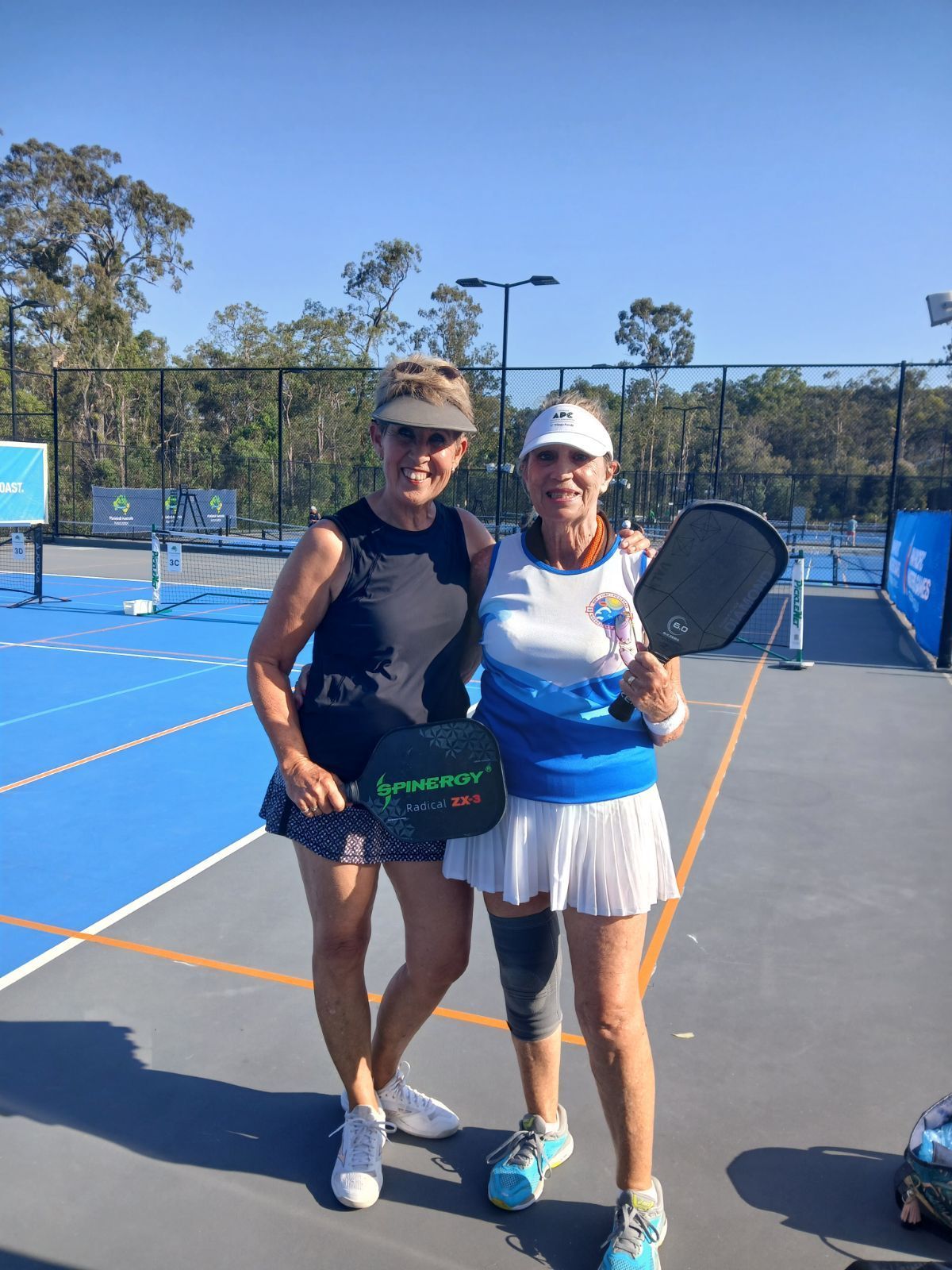 Two women Gold Coast Pickleball members are posing for a picture on a tennis court.