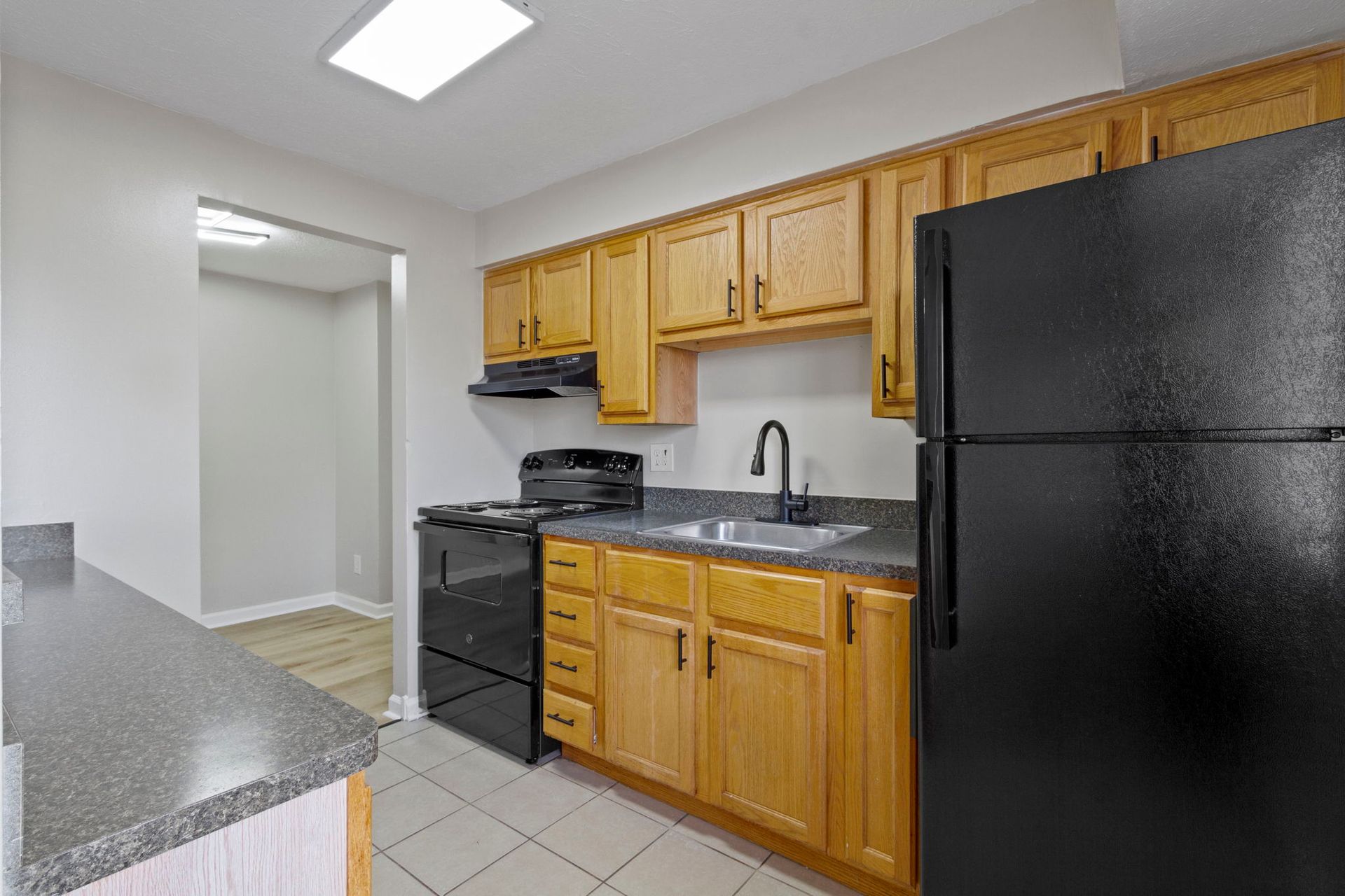 Kitchen with light-colored cabinets, black appliances, and gray countertops. A doorway leads to another room.