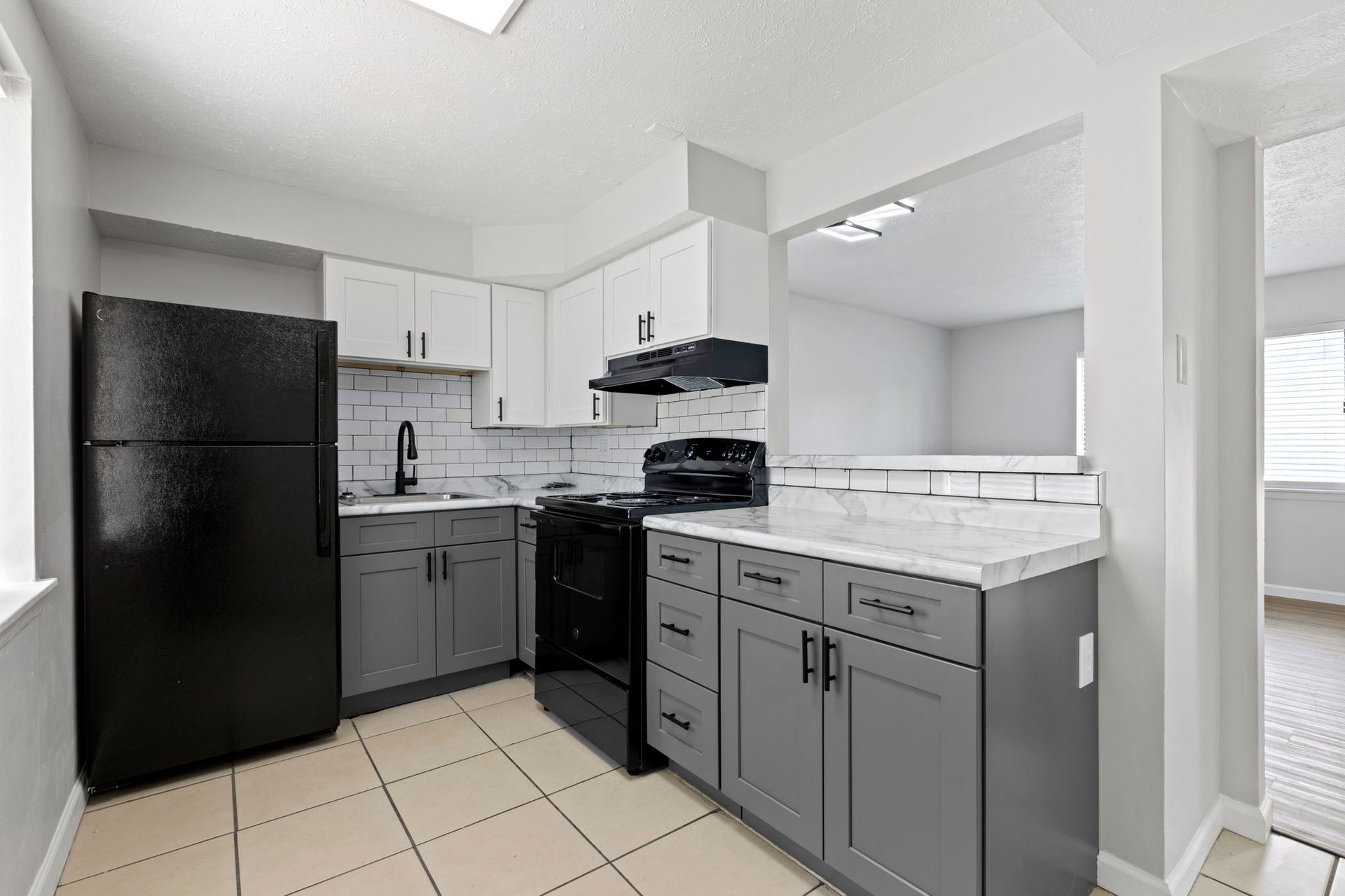 Modern kitchen with gray and white cabinets, black appliances, and light tile floor.