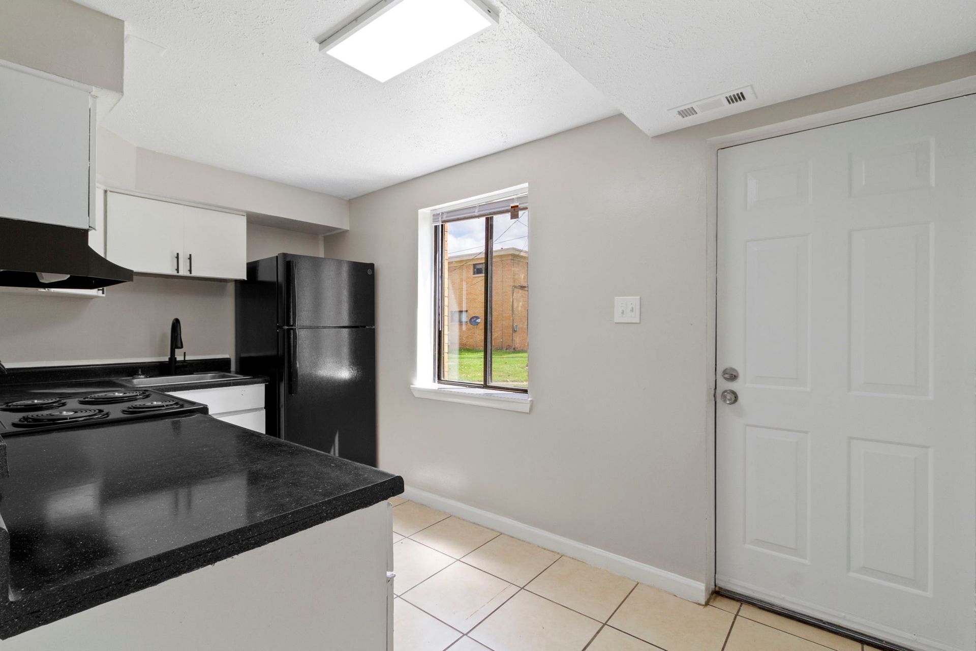 Kitchen with black countertops, white cabinets, black appliances, and a door leading outside.