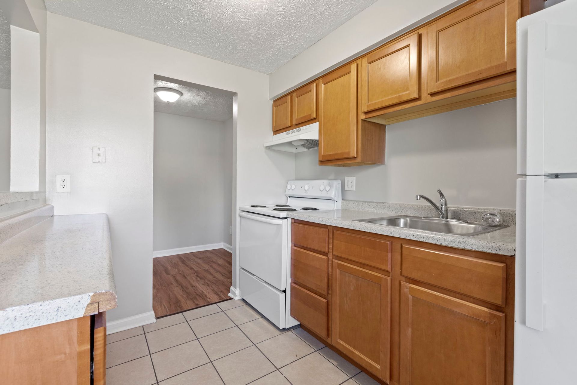Kitchen with wood cabinets, white appliances, and a doorway to another room.
