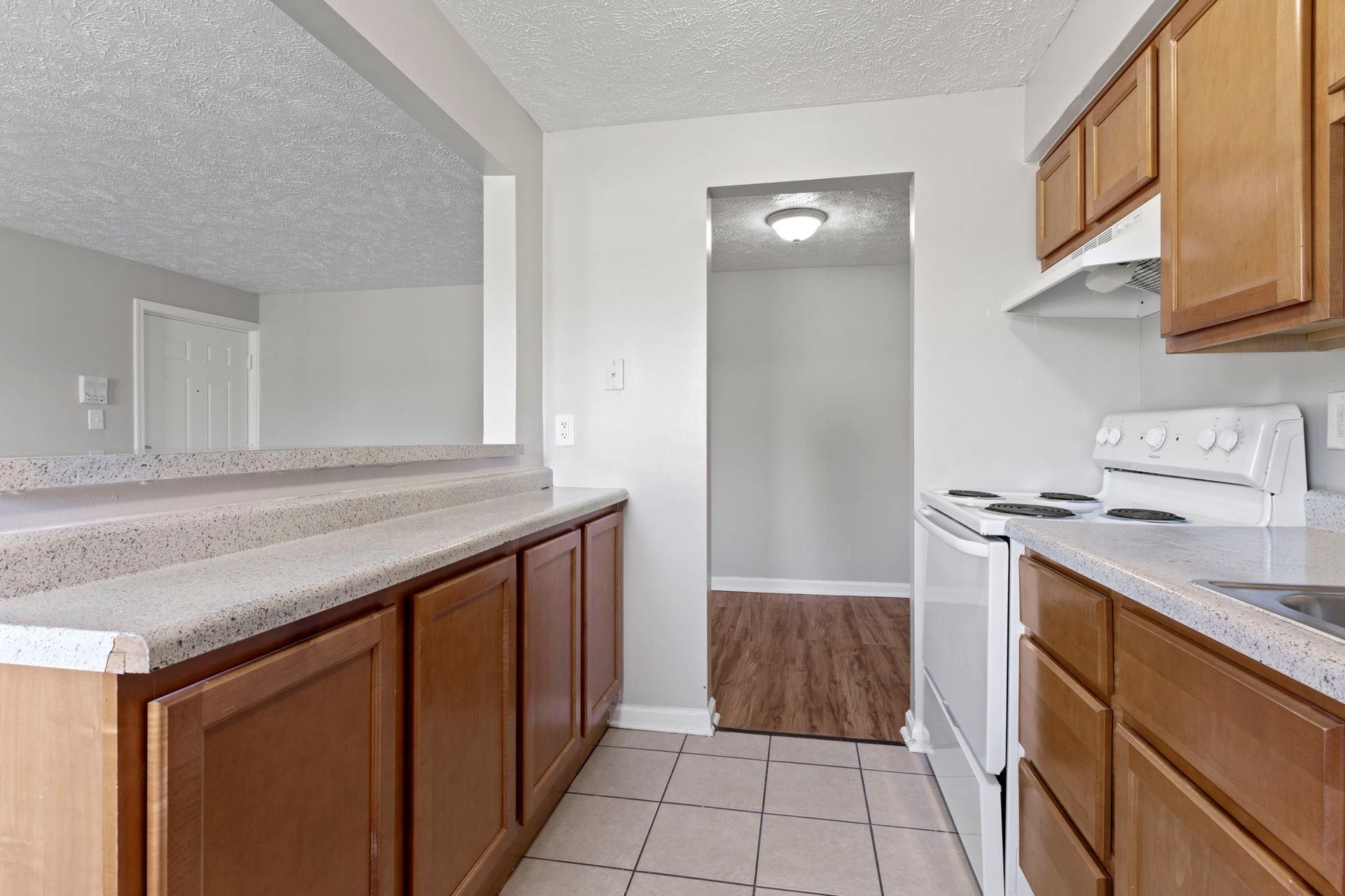 Kitchen with light brown cabinets, white appliances, and a view into another room.