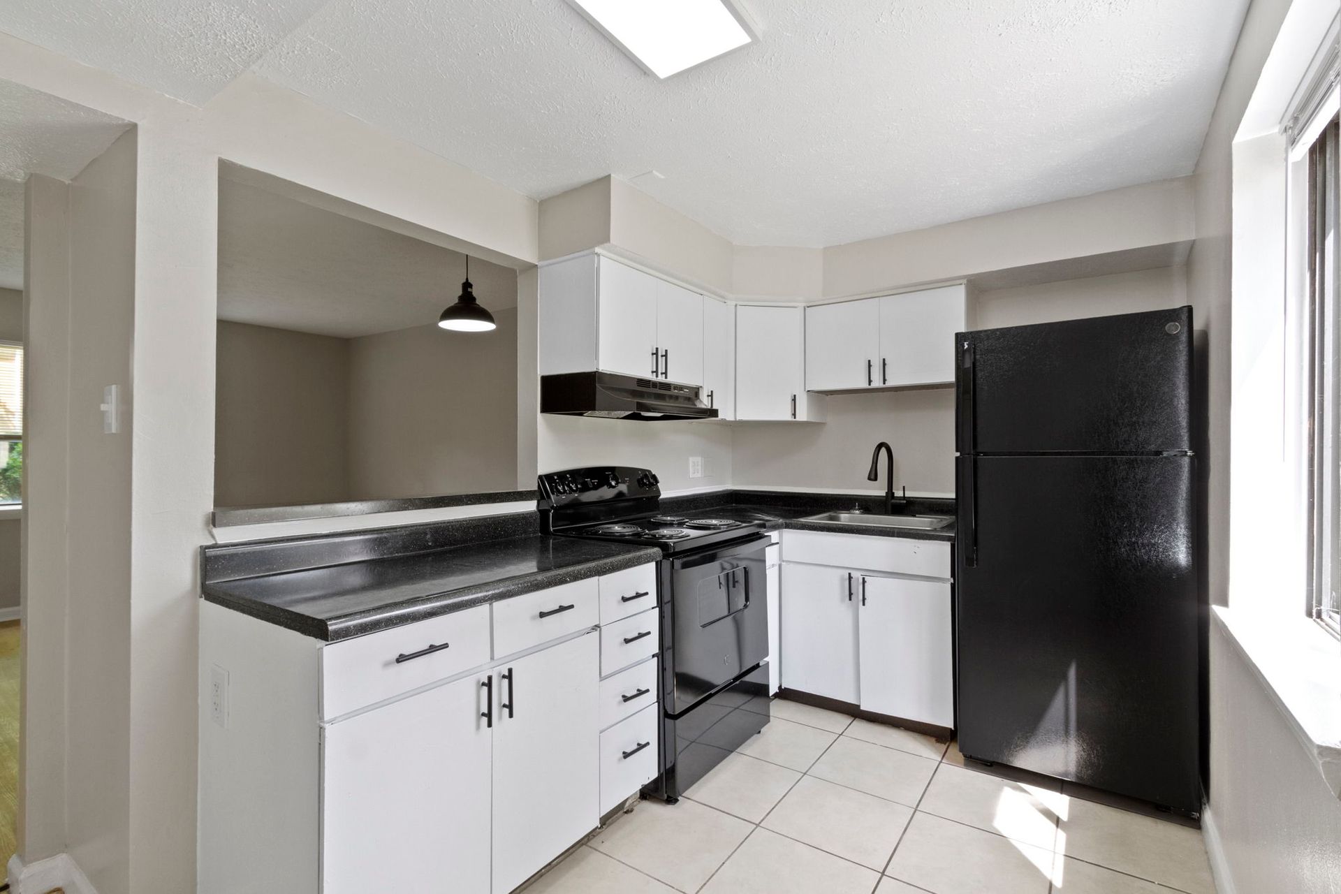 Kitchen with white cabinets, black appliances, and dark countertop, open to another room.