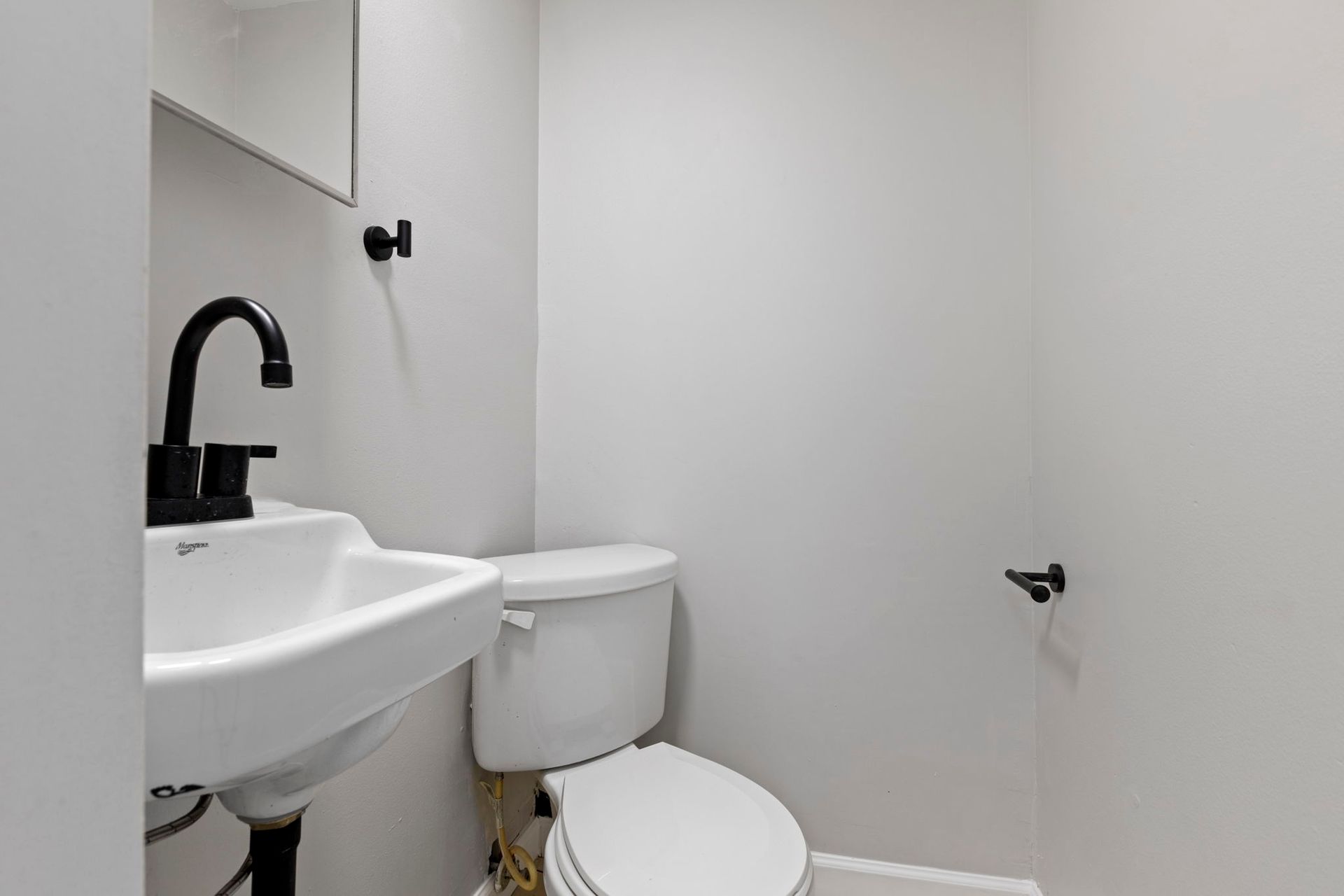 Small white bathroom with a black faucet, toilet, and towel holder; gray walls.