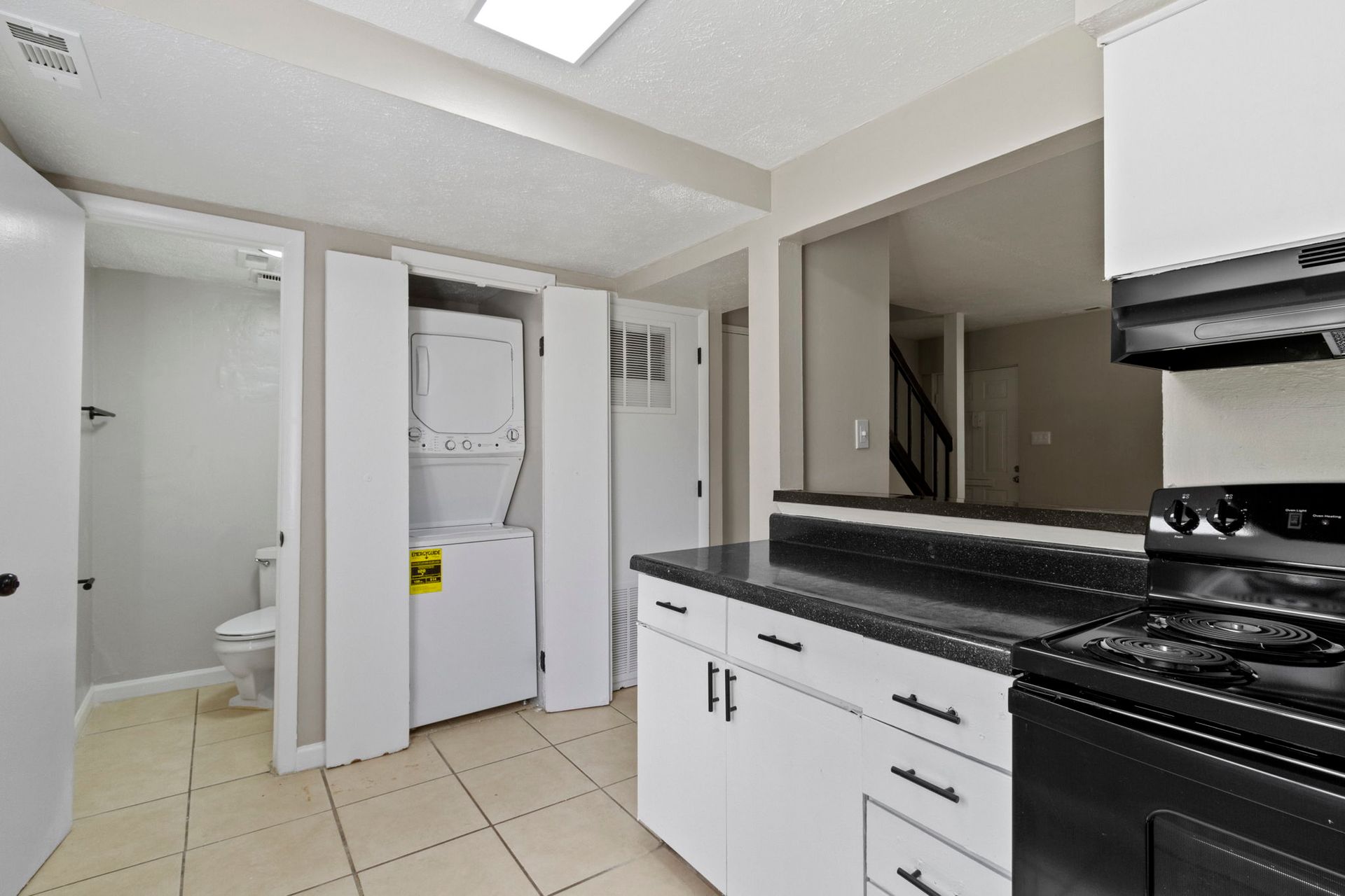 Kitchen with white cabinets, black countertop, and a laundry area with a stacked washer and dryer.