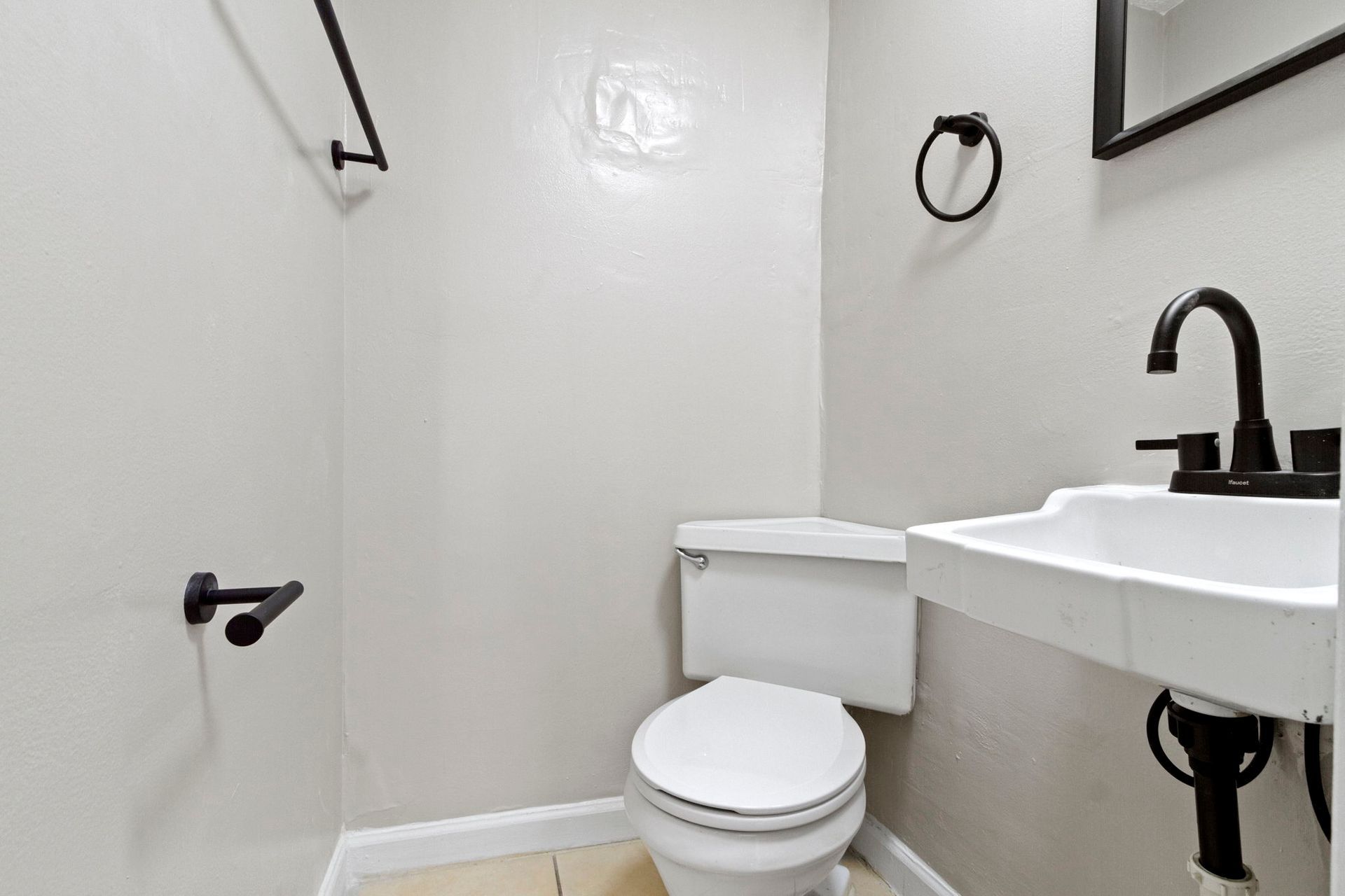 Small, white powder room with toilet, sink, and black fixtures on off-white walls.