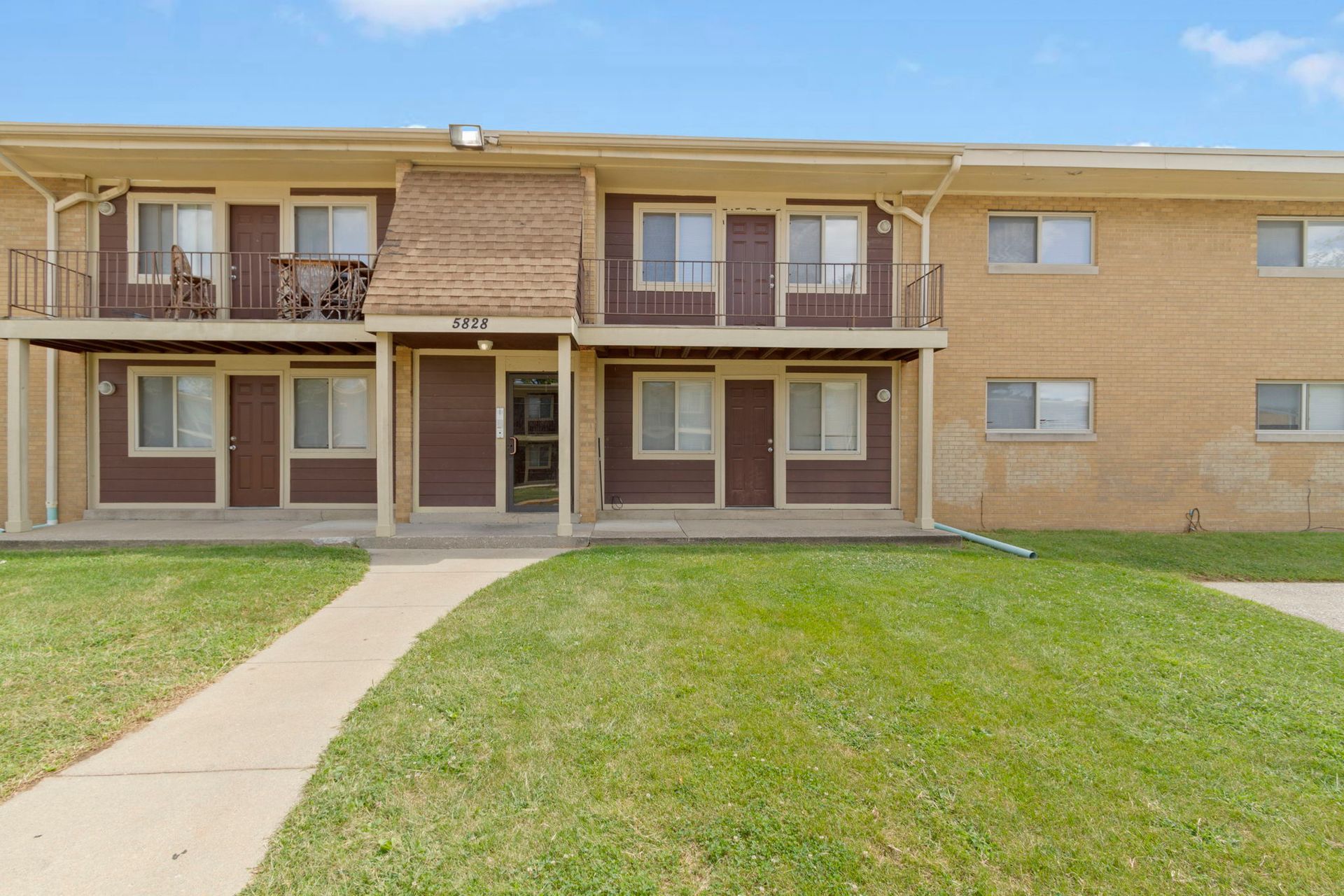 Two-story apartment building with brown doors and trim, a brick center, and green lawn.