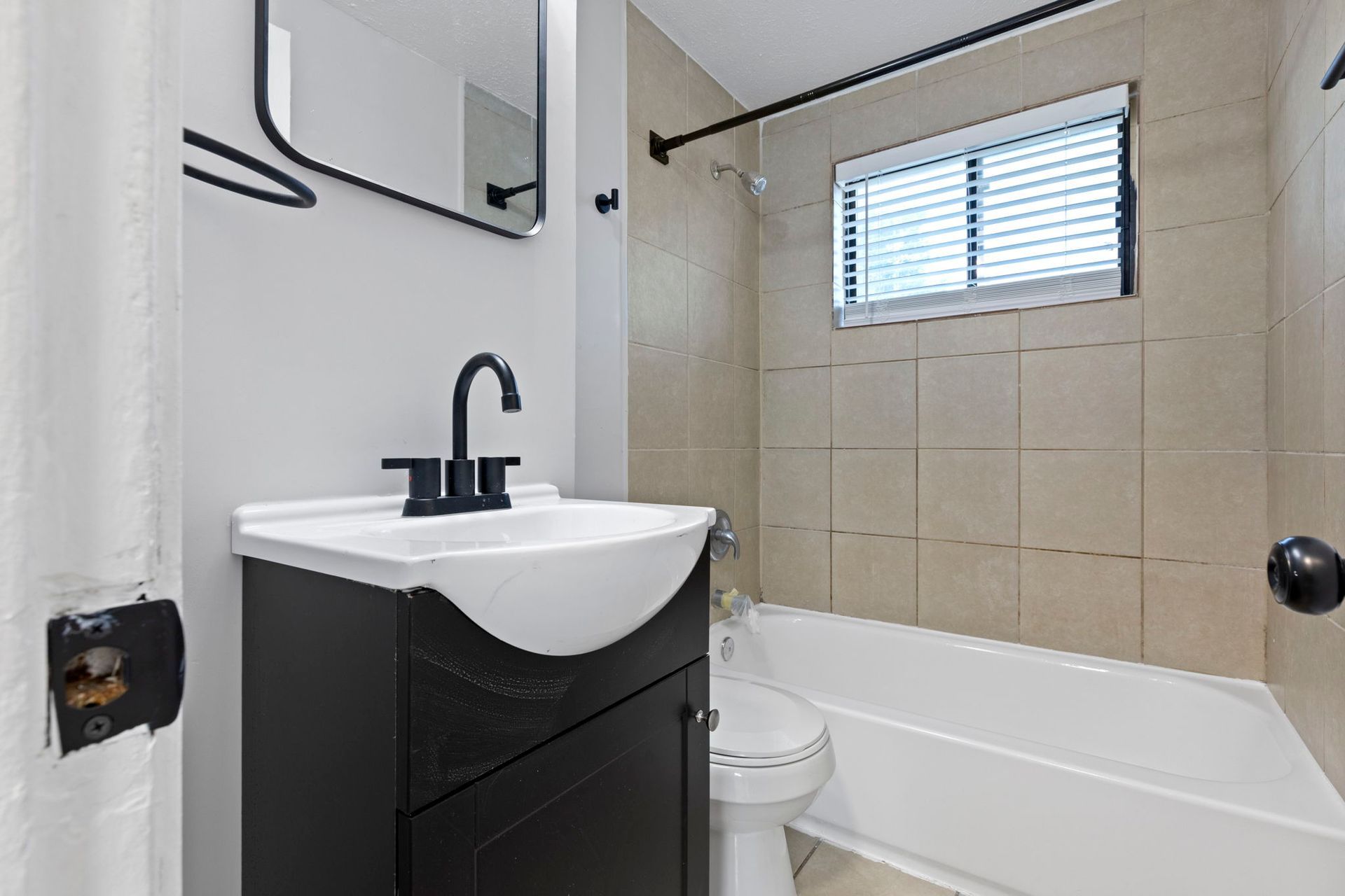 Bathroom with a black vanity, white sink, bathtub, and tan tile surround.