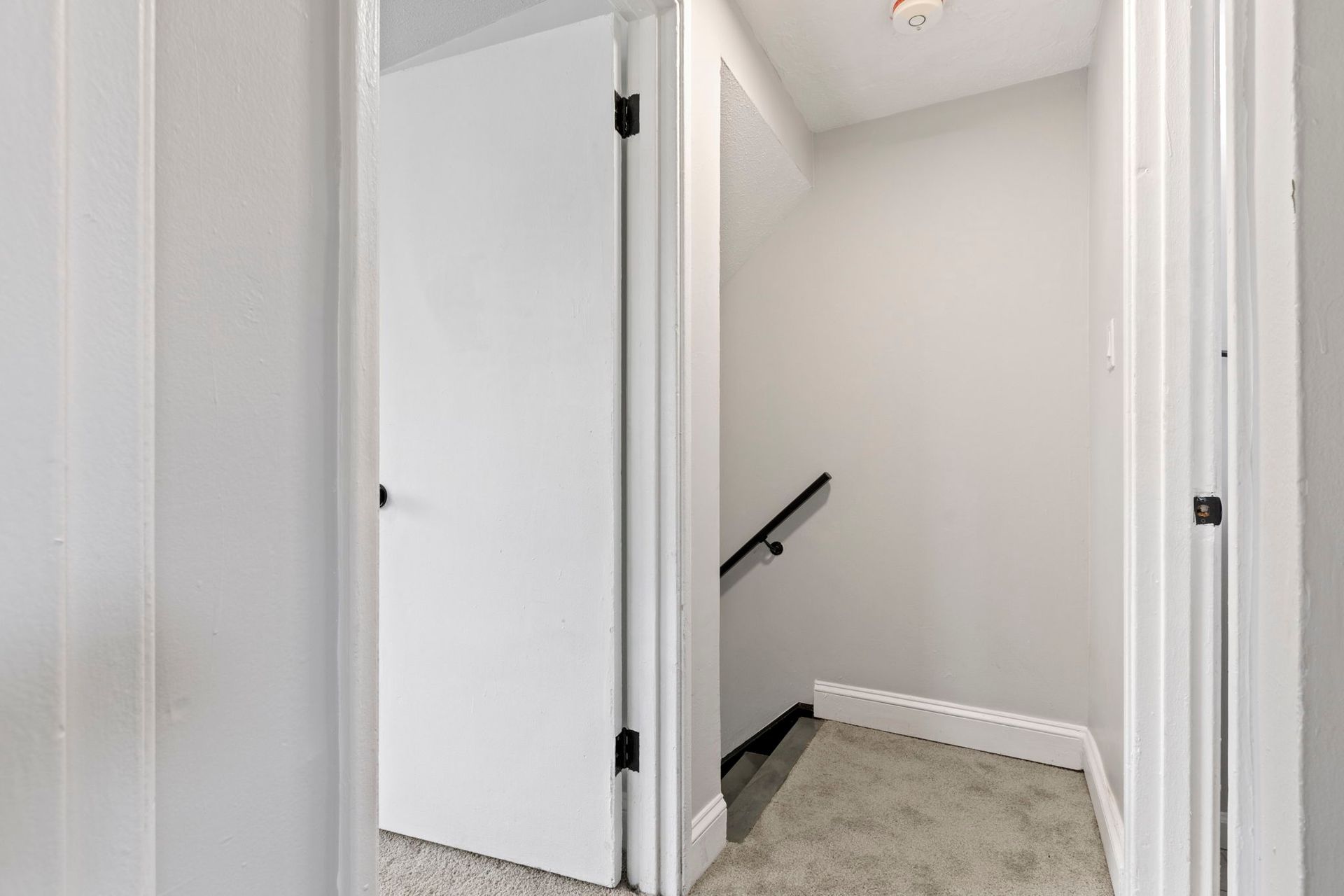Hallway with white doors, leading to a staircase with a black railing. Gray carpet.