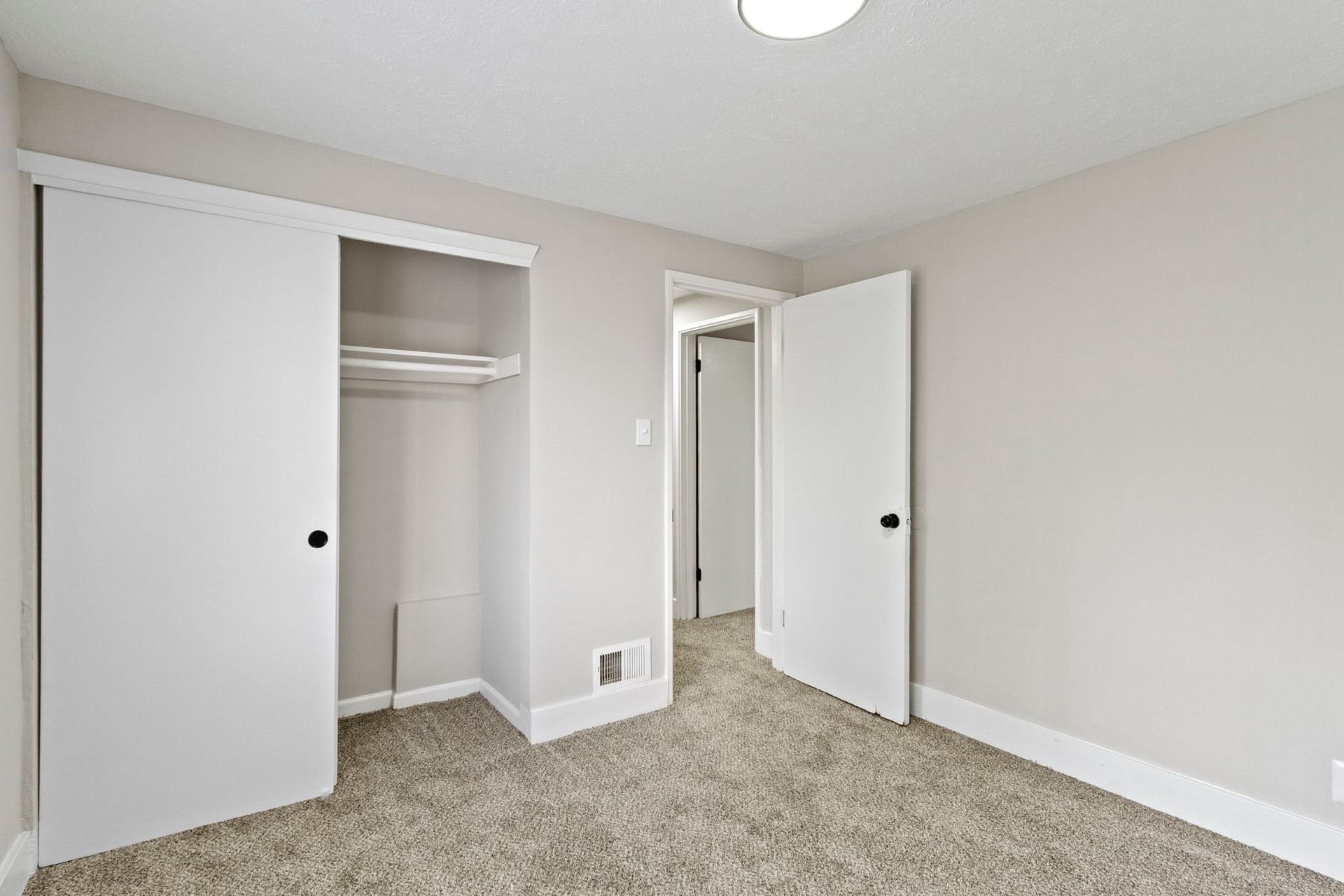 Empty bedroom with carpet, closet, and open door to a hallway, painted light gray.