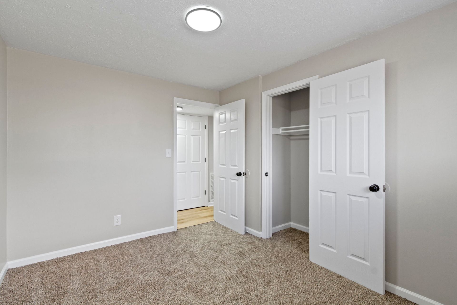 Empty bedroom with beige walls, carpet, and white closet and doors.