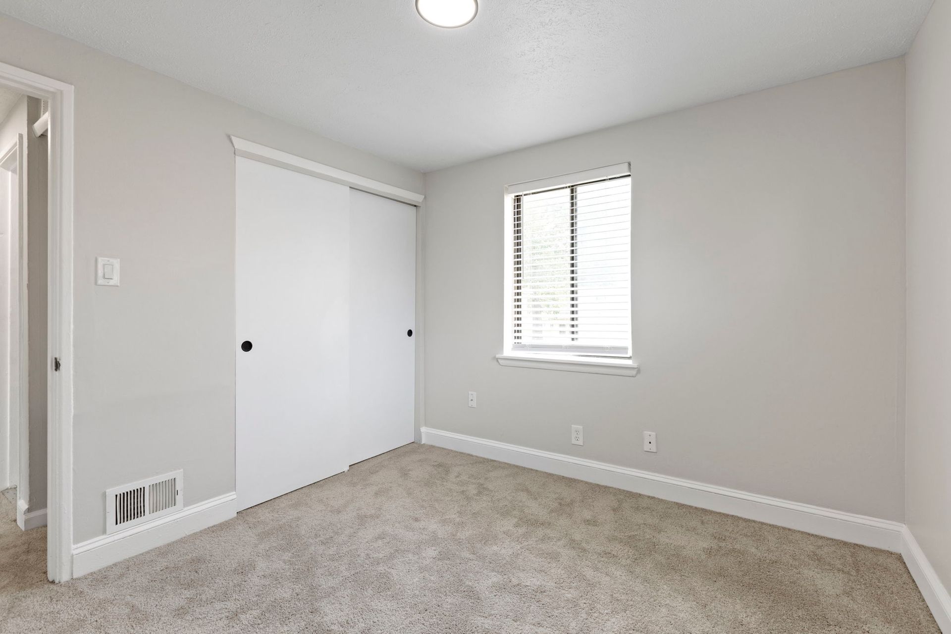Empty bedroom with white walls, carpet, closet, and window with blinds.