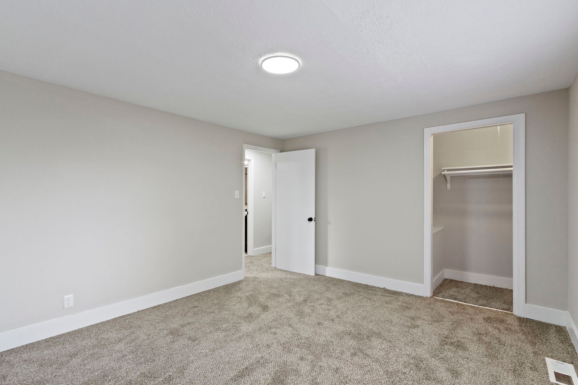 Empty bedroom with gray walls, carpet, and white trim. A closet and door are visible.