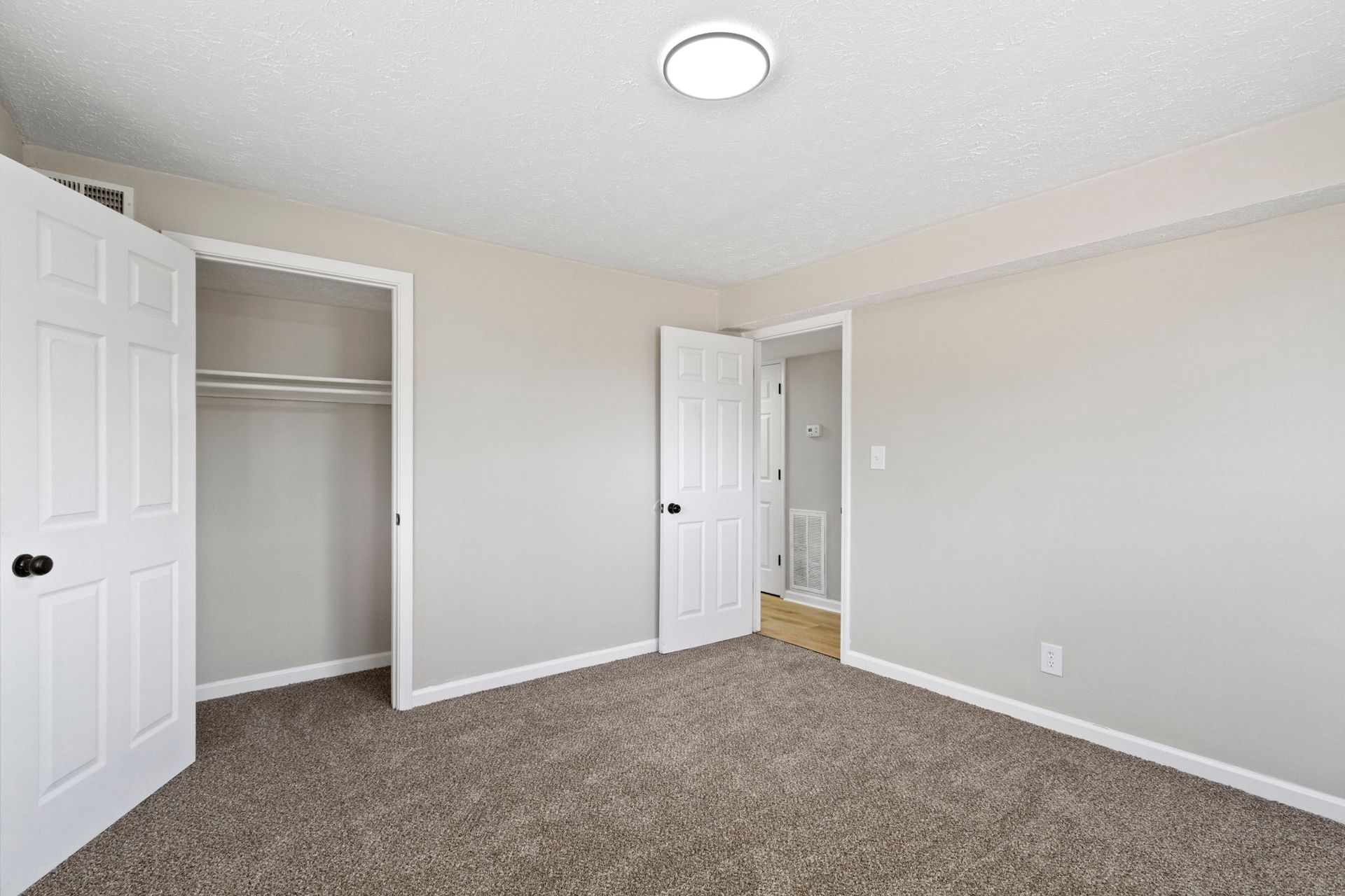 Empty bedroom with open closet and doorway. Gray walls, carpet, and white doors.