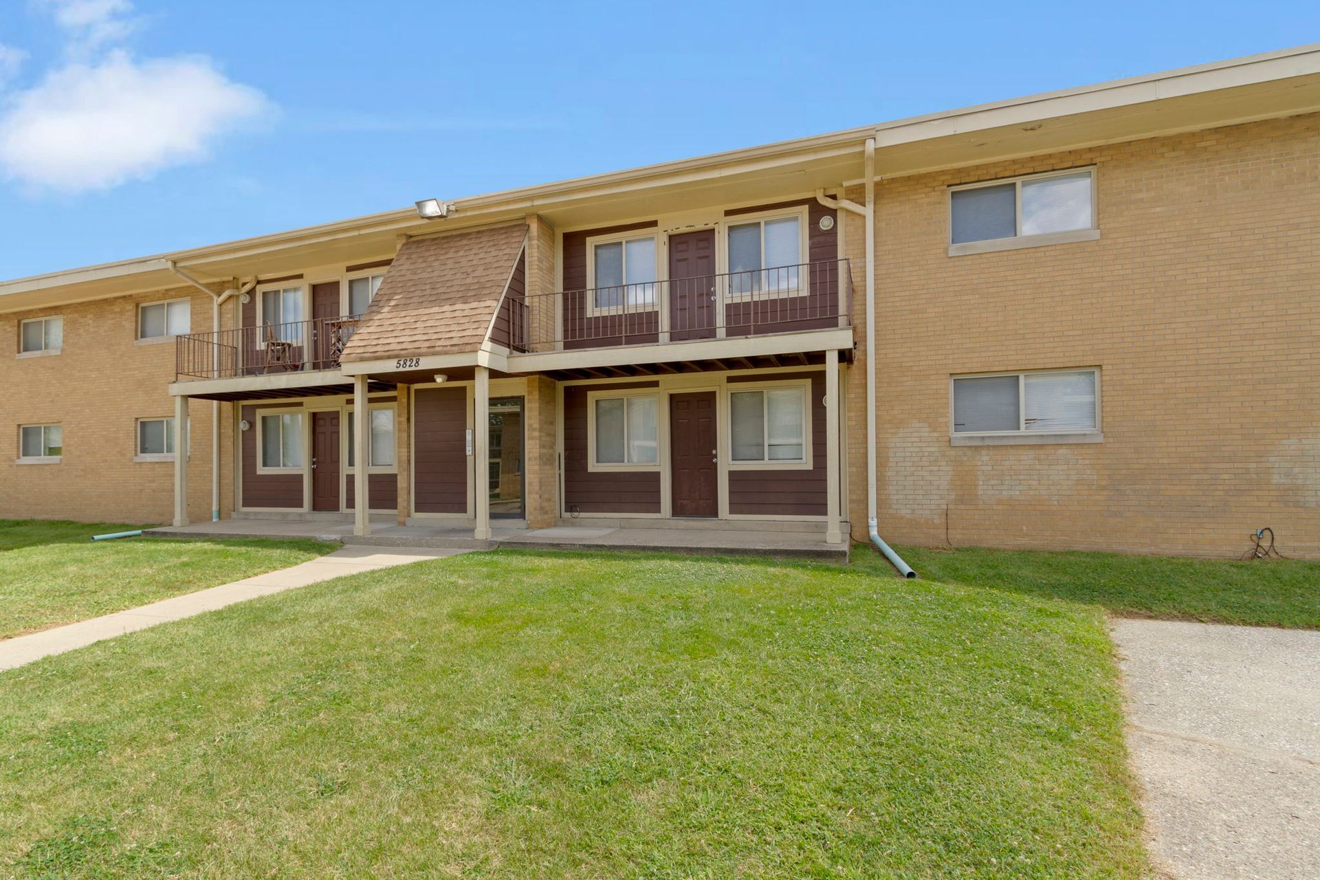 Two-story brown brick apartment building with green lawn and blue sky.