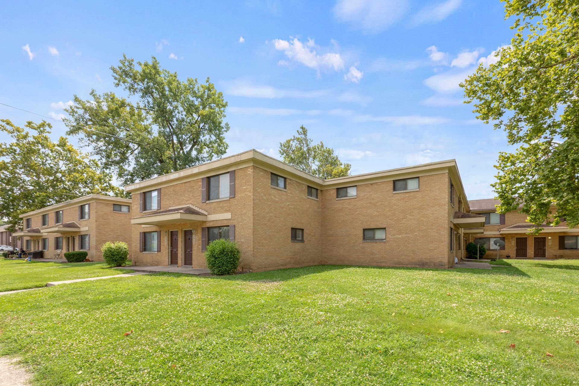 Tan brick apartment buildings with green lawn under a blue sky.