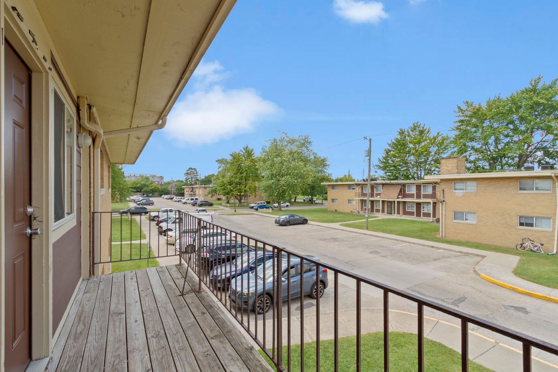 Balcony view of a street lined with parked cars and brick apartment buildings on a sunny day.