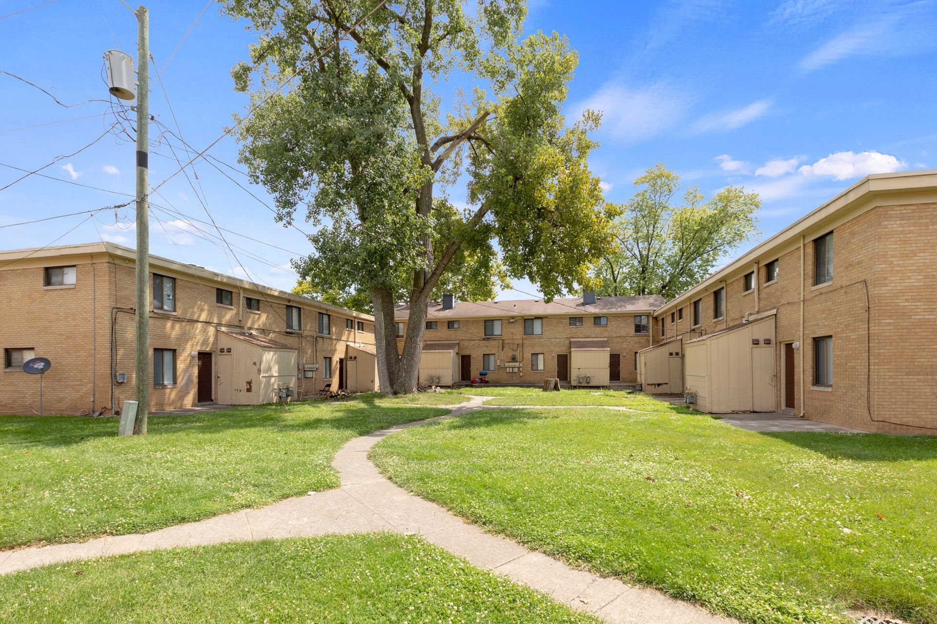 Two-story brick apartment buildings face a grassy courtyard with a tree.