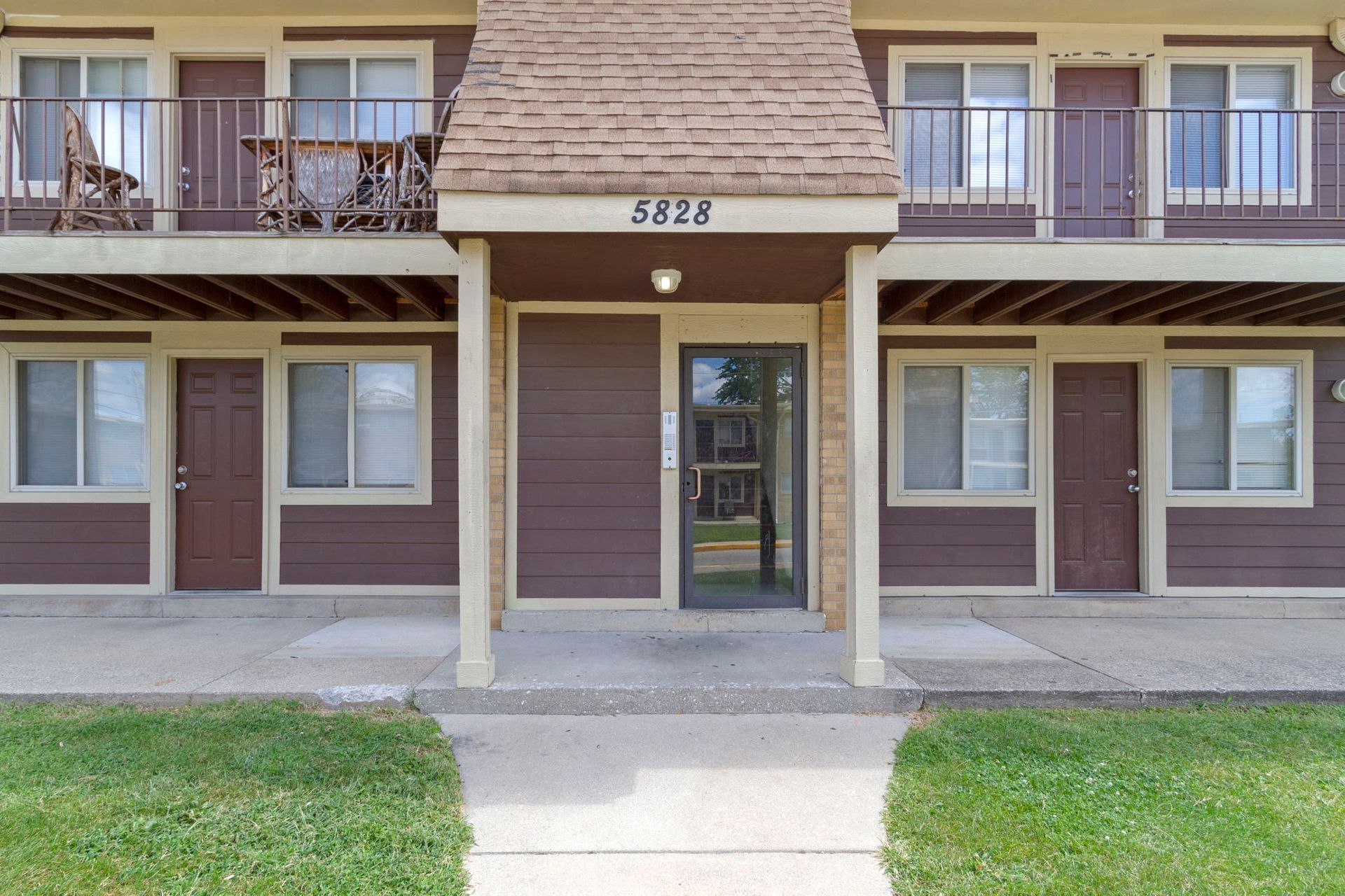 Apartment building exterior with brown siding, balconies, and a central entrance marked