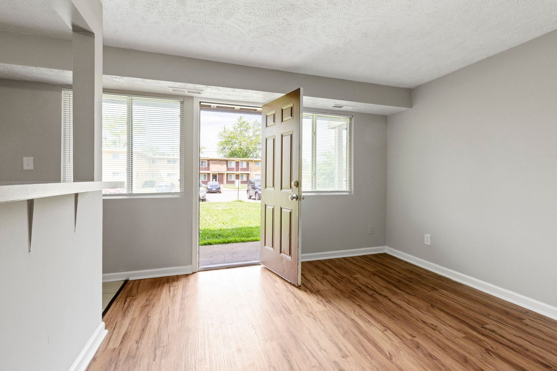 An empty room with wood floors, open door to a grassy area, and light gray walls.
