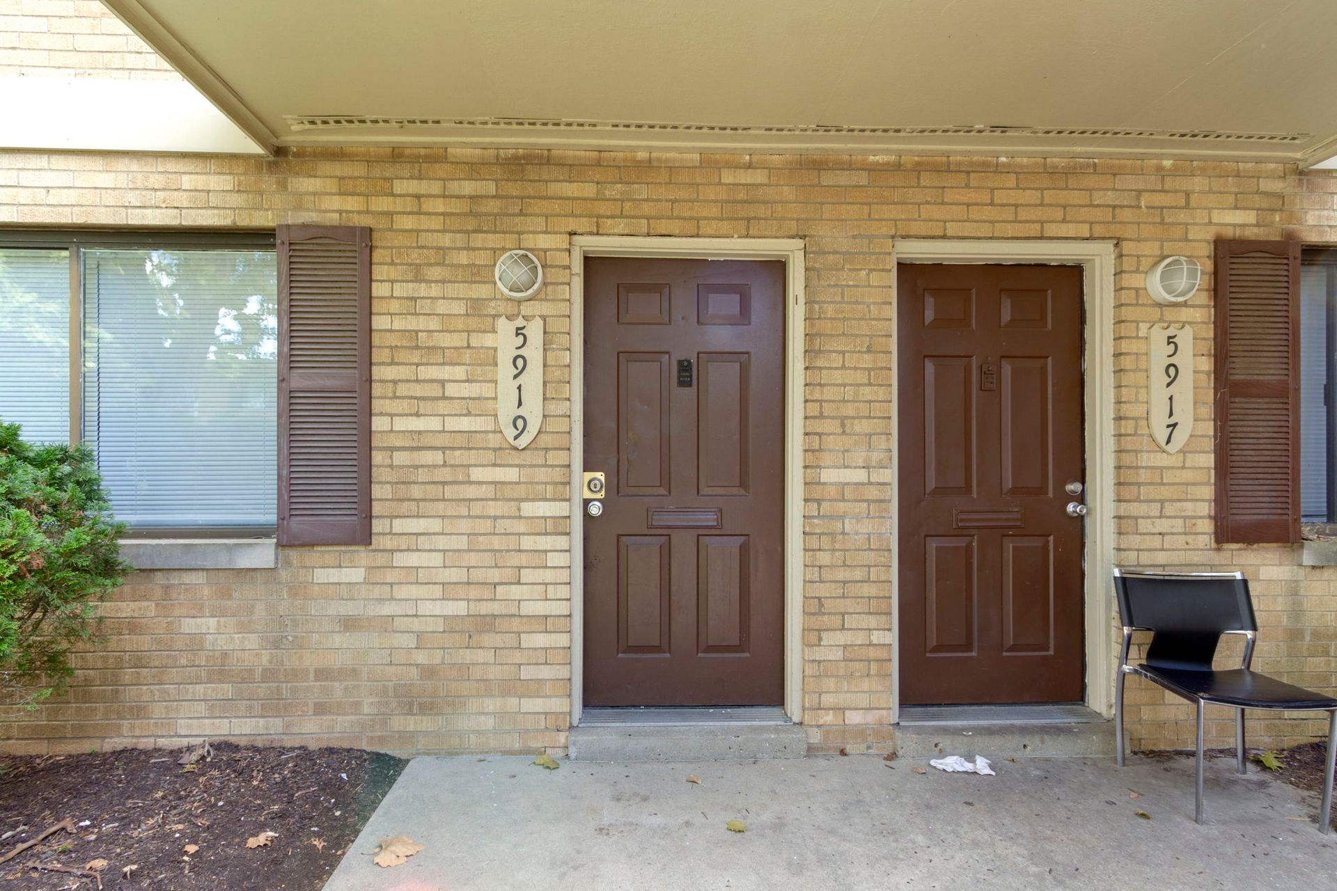 Two brown doors of adjacent units with address numbers on beige brick wall.