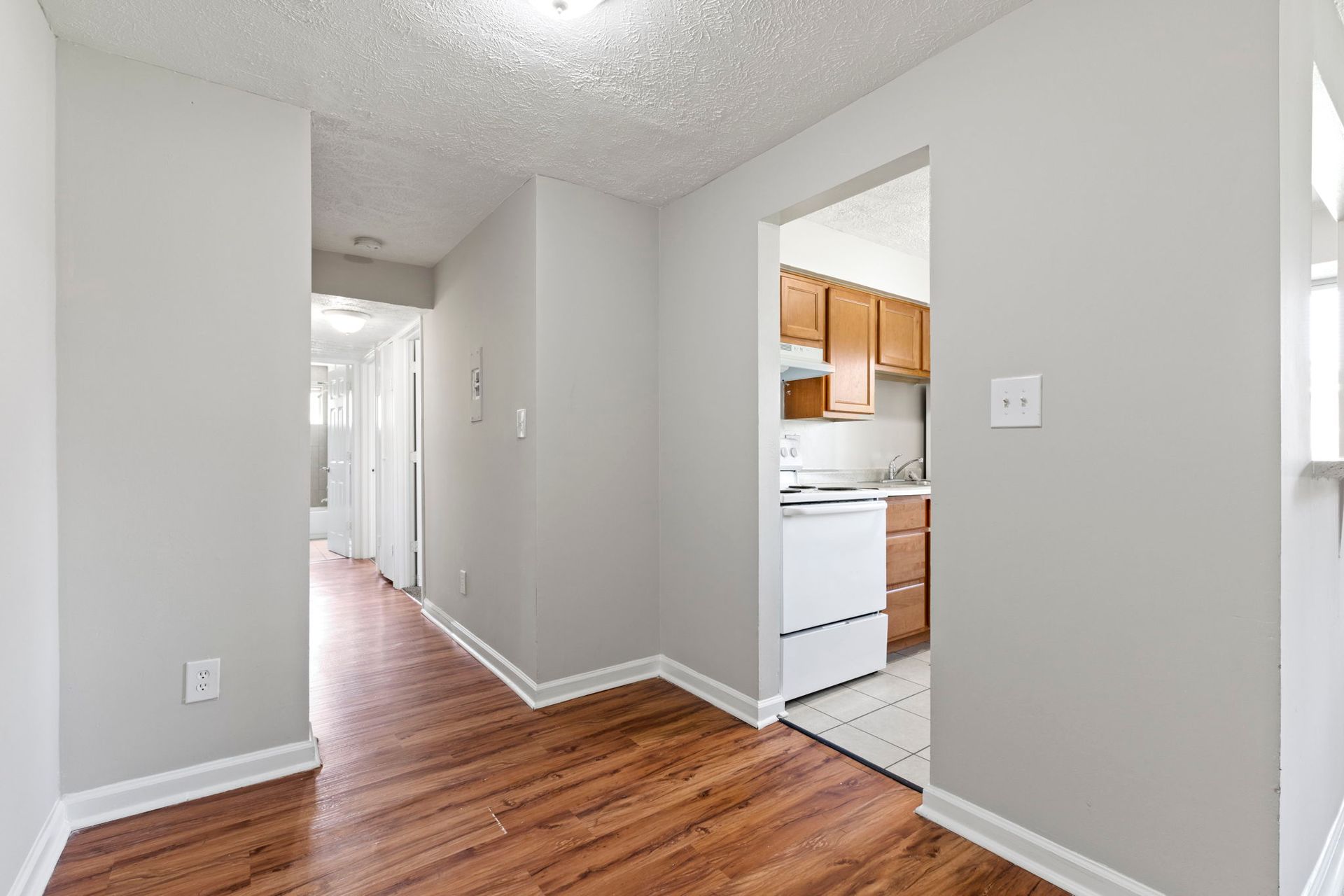 Long hallway with wood floors, light gray walls, and an open doorway to a kitchen.