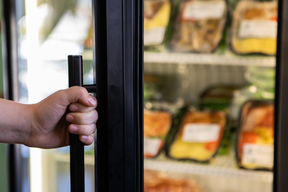 A Person Is Opening A Refrigerator Door In A Grocery Store — NQ Fridge & Freezer Seals In Manoora, QLD