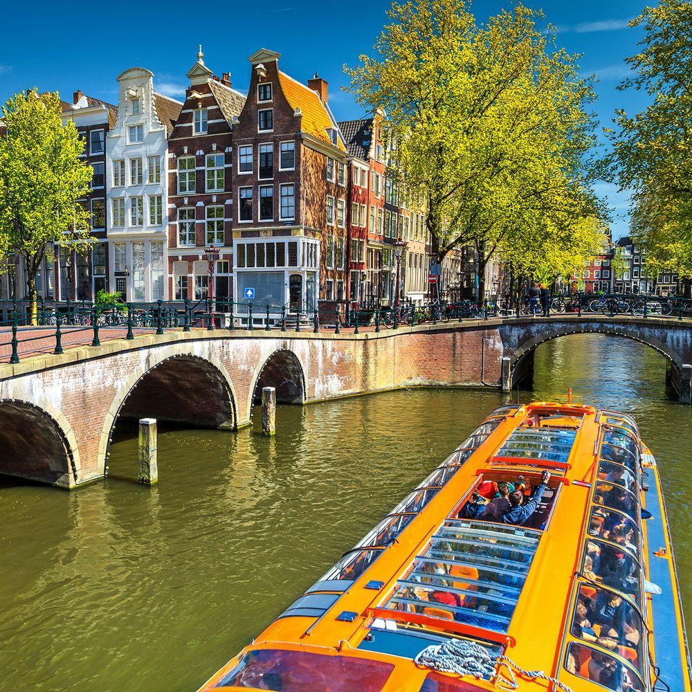 Amsterdam's canal houses with a boat on the canal next to a bridge with trees