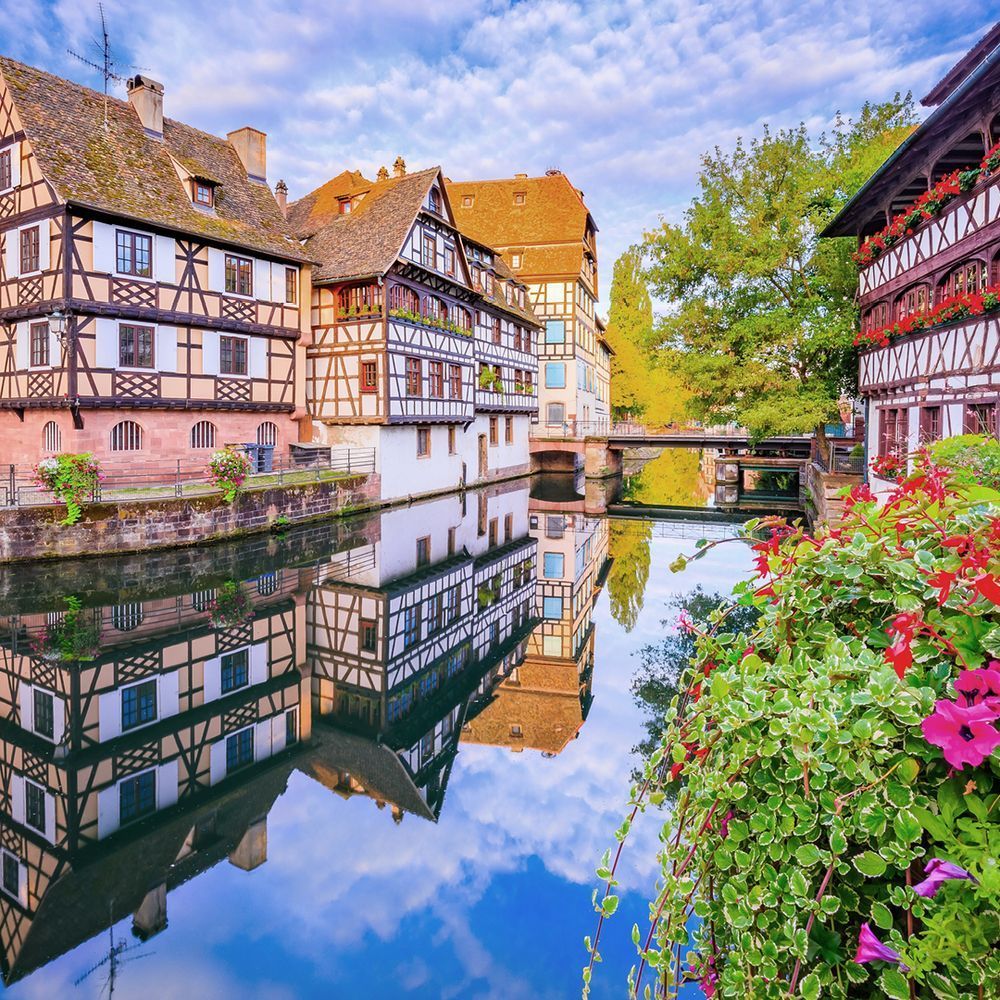 Strasbourg's Petite France with colorful half-timbered houses along a canal with flowers, blue sky and bridge