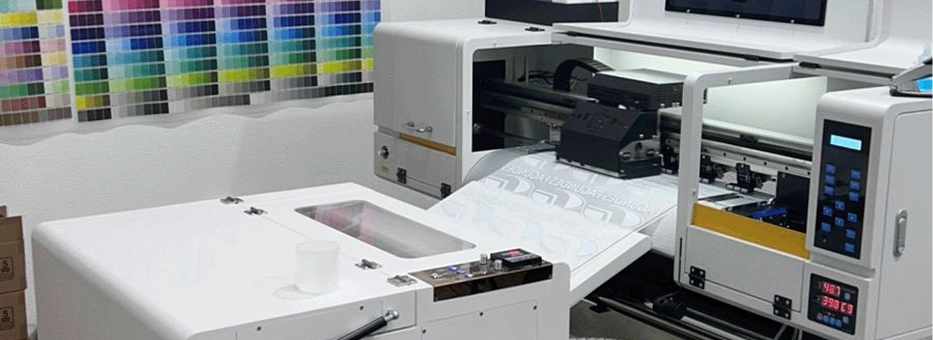 Impressora têxtil digital industrial em uma oficina com uma tabela de cores na parede.
